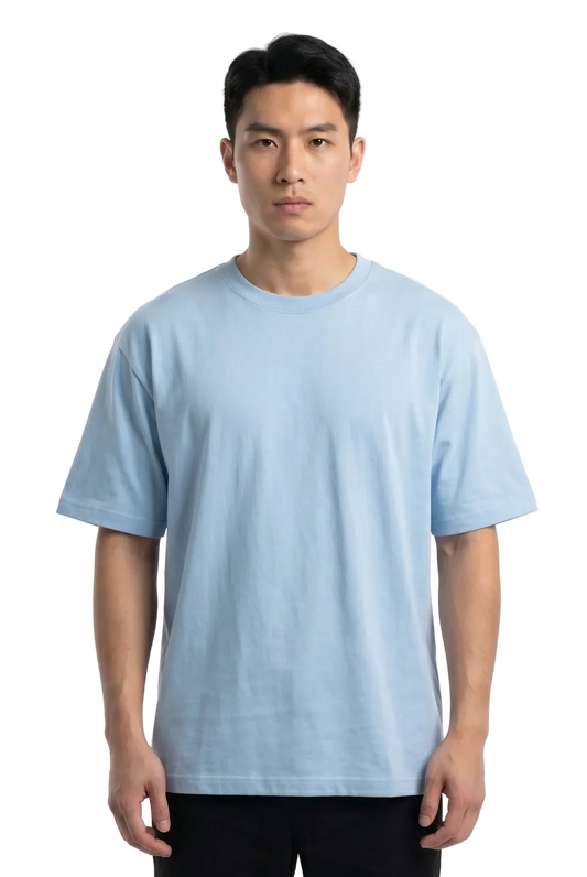 A man wearing a light blue crew-neck t-shirt and black pants, standing against a plain white studio background.