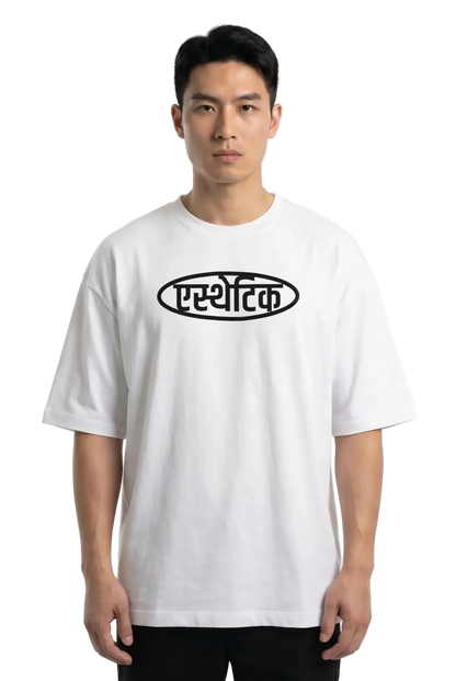 A man wearing a white short-sleeve t-shirt with a black oval graphic containing Devanagari Aesthetic text on the chest, set against a plain white background.