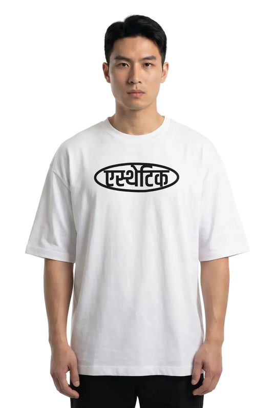 A man wearing a white short-sleeve t-shirt with a black oval graphic containing Devanagari Aesthetic text on the chest, set against a plain white background.