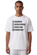 A man wearing a white short-sleeve t-shirt with black printed text reading 'BUSINESS DEVELOPMENT SALES AND MARKETING' inside circular letter boxes, paired with white pants, against a plain white background.
