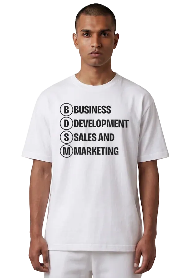A man wearing a white short-sleeve t-shirt with black printed text reading 'BUSINESS DEVELOPMENT SALES AND MARKETING' inside circular letter boxes, paired with white pants, against a plain white background.