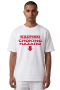 A man wearing a white short-sleeve t-shirt with a red graphic print that reads 'CAUTION CHOKING HAZARD' with a red arrow pointing down, set against a plain white background.