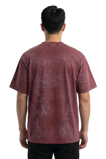 A man viewed from behind wearing a short-sleeve crewneck t-shirt with a washed, mineral-look finish in a dusty rose or mauve color, paired with black pants against a plain white background.