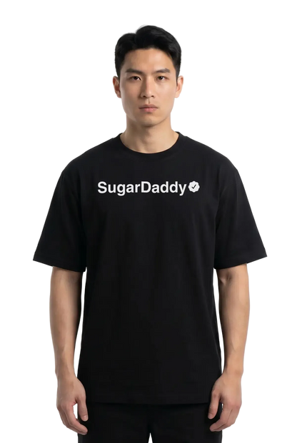 A man wearing a black short-sleeve t-shirt with 'Sugar Daddy' printed in white across the chest, photographed against a plain white studio background.